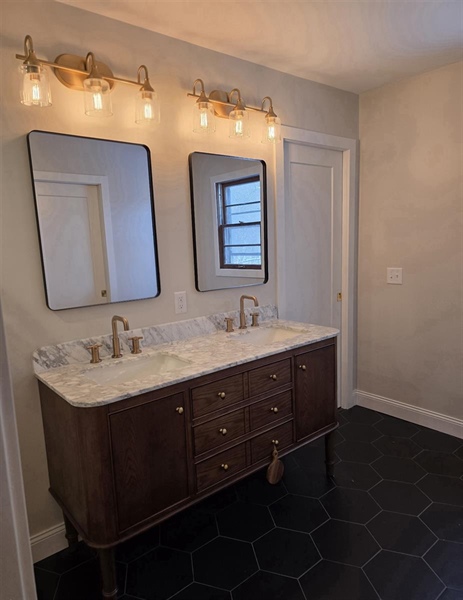 Remodeled primary bathroom in Big Lake, MN with double marble vanity, champagne bronze fixtures and black hexagon tile flooring