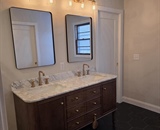 Remodeled primary bathroom in Big Lake, MN with double marble vanity, champagne bronze fixtures and black hexagon tile flooring